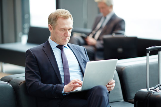 Elegant mature businessman watching webcast in laptop while waiting for airplane in lounge