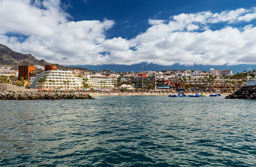 Fototapeta na wymiar Vibrant scenery and deep-blue waters of the Tenerife west coastline as seen from a yacht. The dormant Teide volcano can be seen in the background. Many tourism resorts overlook the coastline.
