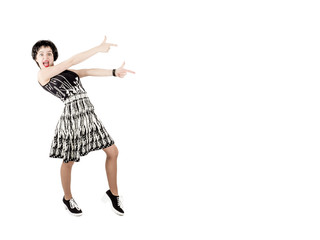Portrait of a cheerful young woman dressed in black and white dress pointing a thumb up at copy space, isolated on white background