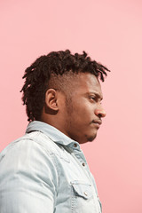 The suspicious business Afro-American man standing and suspiciously looking against pink background. Profile view.