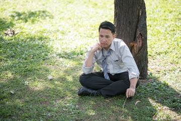 Naklejka na ściany i meble Business man failing and serious under tree in the park. He is stressed with work Unsuccessful disappointed in project