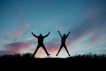 Silhouette of a loving couple. Jumping from happiness couple on top of a hill on a background of the setting sun