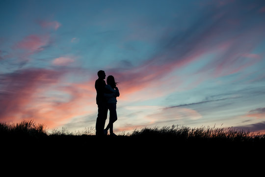 Silhouette of a loving couple hugging on a hill top against the backdrop of the setting sun
