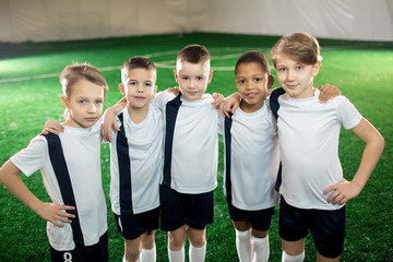 Obraz premium Five affectionate football team members in uniform looking at camera while standing on pitch