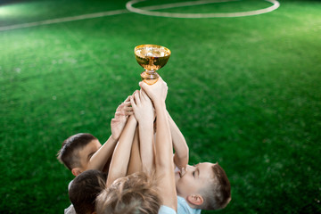 Fototapeta premium Stretched arms of little footballers holding gold award on background of green pitch
