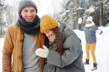 Laughing young couple in winterwear enjoying time with friends in winter park