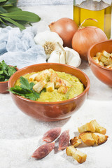 Split pea soup in rustic bowl decorated with fresh green leaves,garlic and slices of lard