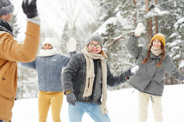 Fototapeta na wymiar Happy young friends in winterwear playing snowballs on snowy winter day