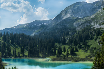 Fototapeta na wymiar Amazing alpine scenery with vivid turquoise colored lake in foreground and pine forest covering a wonderful mountain meadow