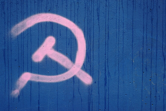 Hammer und Sichel an der Mauer / Das Symbol Hammer und Sichel der Staatsflagge ehemaligen Sowjetunion und des Kommunismus an einer blauen Mauer.