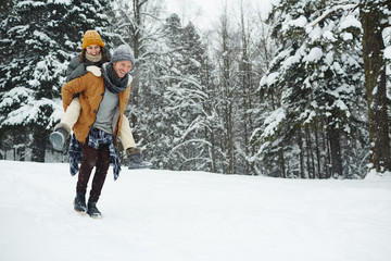 Happy girl sitting on back of her boyfriend while having fun in winter forest