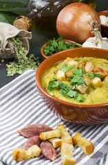 Split pea soup in rustic bowl decorated with fresh green leaves,garlic and slices of lard