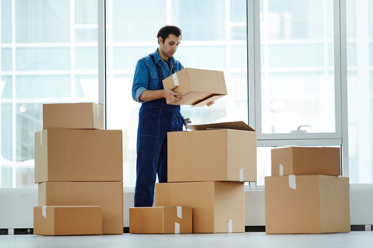 Delivery man in uniform putting packed boxes on each other by office window