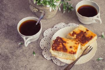 A delicious homemade dessert. Sweet curd pudding on a white plate, next to a cup of coffee and a pot of flower.  Toned photo.