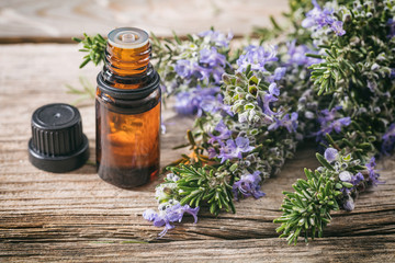 Rosemary essential oil and fresh blooming twig on a wooden table, closeup view