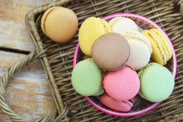Colorful macaroons in bowl on wicker surface
