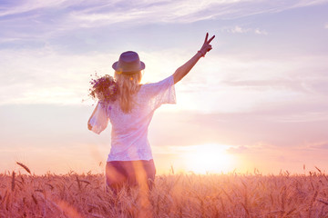 Teenage girl feels freedom and relaxing outdoors, enjoying nature with the sunrise field of wheat. The concept of freedom and happiness.