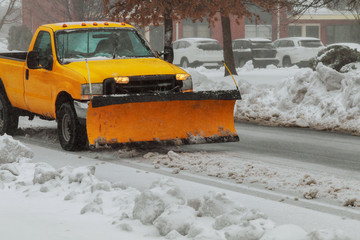 Snow plough truck clearing road after whiteout winter snowstorm blizzard for vehicle access