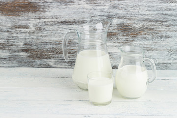 Milk in the glass jugs, white wooden background