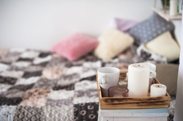 Fototapeta na wymiar Beautiful spring decorated interior in white textured colors. Bedroom, bed on wooden pallets. A cup for tea or coffee and a candle on a tray.