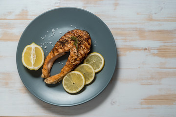 Salmon fillet. Grilled salmon with herb and lemon on plate. Fish roasted on a wooden background.