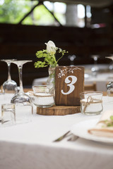 Simple but luxury rich table setting for a wedding celebration in nice cozy restaurant. Wineglasses, plates and bouquet of summer seasonal flowers on a table. Sunlight from a window. Copy space