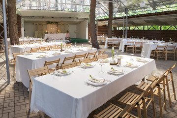 Simple but luxury rich table setting for a wedding celebration in nice cozy restaurant. Wineglasses, plates and bouquet of summer seasonal flowers on a table. Sunlight from a window. Copy space