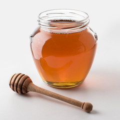 Honey dipper and honey in jar on white background.