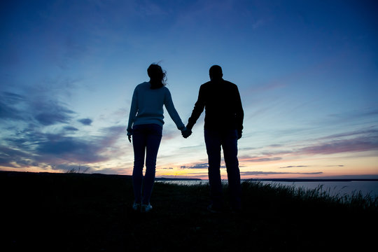 Silhouette of a loving couple who holds hands on the background of the setting sun