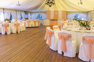 Simple but luxury rich table setting for a wedding celebration in nice cozy restaurant. Wineglasses, plates and bouquet of summer seasonal flowers on a table. Sunlight from a window. Copy space
