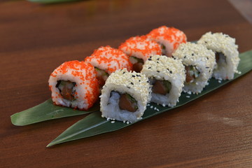Sushi roll with salmon and shrimp tempura on the leaf. wodden background