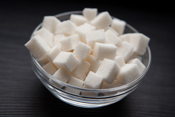 Fototapeta na wymiar White sugar cubes in glass bowl on black