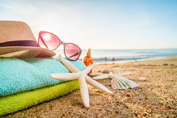 Sunglasses, towels, hat, sun block, shells and starfish on sandy beach