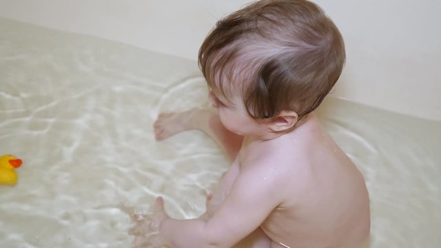baby is playing in water with toys, child is bathing in clean water in bathroom