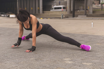 Brunette slim adult sexy fit sporty caucasian woman in sportswear on a european city streets in morning do exercises (workout), stretch her legs and butt. Copy space