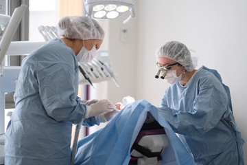 Doctor and assistant during the installation of the implants to the patient in a dental clinic