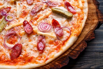 Close up texture of hot pizza with salami, onions and gherkins served on chopped wood. Food background