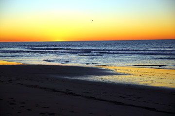 Vibrant orange and yellow sunset as seen from sandy beach on calm day along Pacific Ocean coast