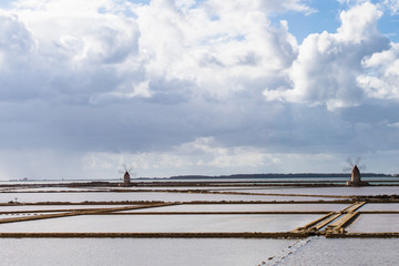 Marsala,Trapani - Sicilian salt lakes with wind mills and salt piles, during a sunny day with blue sky and clouds.