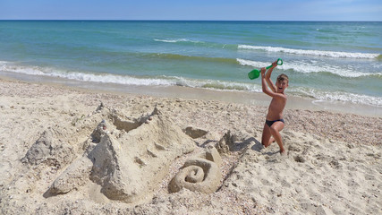 Naklejka na ściany i meble boy teenager is building on the beach sand castle