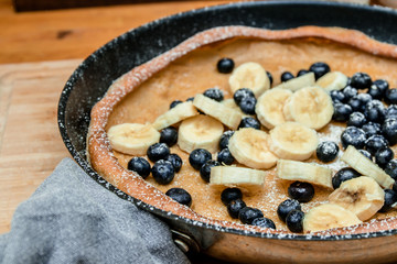 Dutch Baby pancake with blueberries, banana and powdered sugar baked in oven