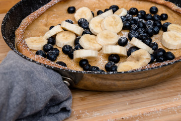 Dutch Baby pancake with blueberries, banana and powdered sugar baked in oven