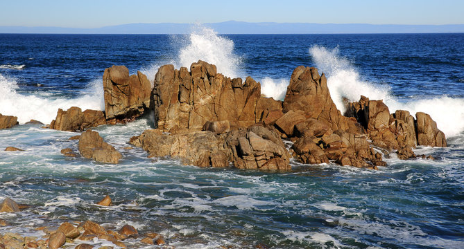 White waves crash against rugged rocks in Monterey, California's coastline