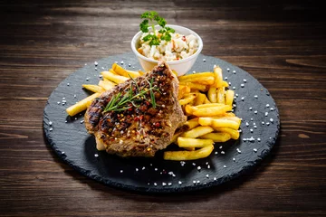 Zelfklevend Fotobehang Grilled steak with french fries and vegetables served on black stone on wooden table  © Jacek Chabraszewski