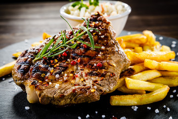 Grilled steak with french fries and vegetables served on black stone on wooden table 