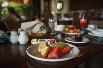On the breakfast table there is a plate with sliced exotic fruits, desserts and devices.