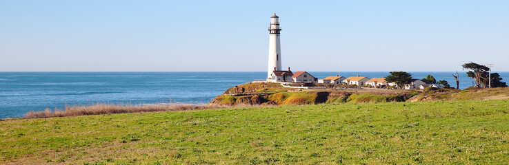 White lighthouse towers over green grass and blue ocean waters along Pacific Coast
