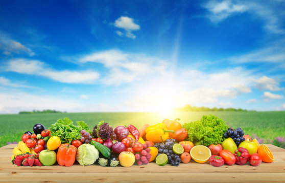 Vegetables and fruit on wooden table of boards against background of spring field