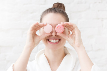 Funny, pretty young woman making glasses with colorful macarons, holding pink macaroons in front of eyes