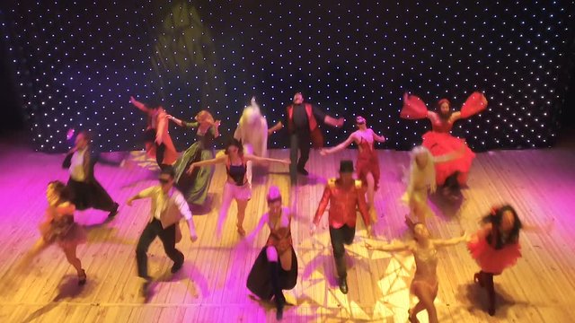 People in bright costumes are dancing in the modern theatre